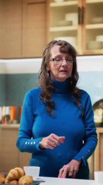 Ev mutfağında dikilen yaşlı insanların dikey video portresi kahve ve neşeli gülümsemelerle, ev işlerinden ve sabah rutin anlarından keyif alarak. Huzurlu bir yaşam tarzı, doğal ve tatmin edici bir yaşam. Kamera B