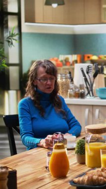 Dikey video yaşlı karı koca kahvaltı masasında sabah rutininin keyfini çıkarıyorlar, birlikte kahve servisi yapıyorlar ve dizüstü bilgisayarla internette dolaşıyorlar. Emeklilik süresince neşeli bağlılık ve doğal yaşam tarzı