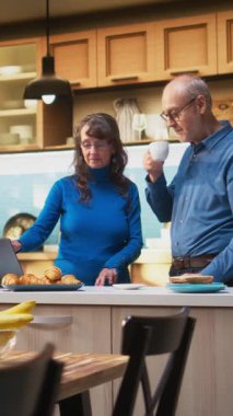 Dikey Video Yaşlıları, ev mutfağında dizüstü bilgisayarda gezinen ve bir fincan kahve ve huzurlu rahatlama keyfi yapan bir çift ile evlendi. Neşeli bir yaşam tarzı, mutlu ve rahat anlar.