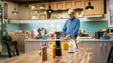 Üst düzey koca, bilgisayarında parlak bir mutfakta web sitelerine kayıyor ve sabah kahvesini yudumlarken sakin bir anın tadını çıkarıyor. Huzurlu bir emeklilik ve mutlu bir yaşam tarzı. Kamera A.