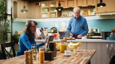 Yaşlı yetişkin erkek, kırsal mutfak alanında dizüstü bilgisayarda geziniyor, sabah kahvesiyle rahat bir anın tadını çıkarıyor. Huzurlu bir emeklilik ve mutlu bir yaşam tarzı. Kamera A.