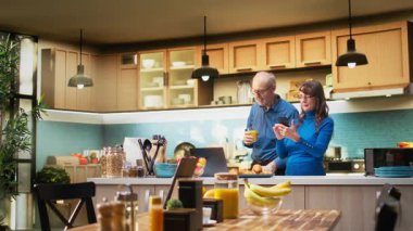 Üst düzey bir kadın akıllı telefonuyla internet sitelerinde geziniyor ve mutfakta gülümsüyor, kahveyle rahatlıyor ve huzurlu emeklilik hayatının tadını çıkarıyor. Emeklilik, pozitif yaşam tarzı ve sabah rutini. Kamera A.