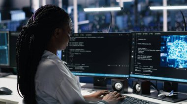 Veri merkezi sistem yöneticisi sinirsel ağ yazılım geliştirme üzerinde çalışıyor. Sunucu odasında Afrikalı Amerikalı bir kadın bilgisayar, kamera A kullanarak makine öğrenme teknolojisi uyguluyor.