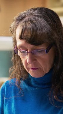 Mutfakta gülümseyen ve sıcak içkinin keyfini çıkaran yaşlı kadının dikey video portresi. Emekli hayatın doğal portresi huzurlu yaşam tarzını ve evdeki rahatlığı yansıtıyor.