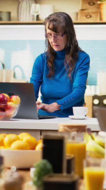 Dikey video yetişkin internette akıllı telefondan geziniyor ve mutfakta gülümsüyor, kahveyle rahatlıyor ve huzurlu emekliliğin tadını çıkarıyor. Emeklilik, pozitif yaşam tarzı ve doğal ev hayatı.