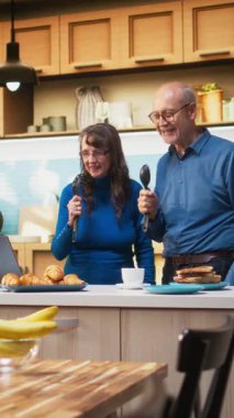 Dikey Video delisi yaşlı çift mutfakta mikrofon olarak aletlerle birlikte şarkı söylüyor, emeklilik sırasında sevgi ve neşeli enerji gösteriyorlar. Etrafta dolaşıp müzikle eğlenmek.