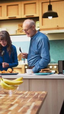 Dikey Video Aşırı neşeli yaşlı evli çift karaoke söylüyor ve mutfakta kendilerini genç hissediyorlar, pozitif enerji ve eğlence. İnsanlar sevgi dolu bir bağ kurup keyifli bir ortam yaratıyorlar.