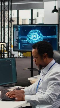 Ofisteki dikey video teknisyeni yapay zeka LLM sohbet robotu cevapları ile görevleri çözüyor. İşteki Afrikalı Amerikalı adam büyük dil model programıyla etkileşim kurmak için PC kullanıyor