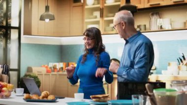 Mutfakta dans eden ve sabah müziğinin keyfini çıkaran eğlenceli yaşlı insanlar. Romantik tutku, mutluluk ve evde sevgi dolu bir ilişkinin güzelliğini gösteren havalı ve şapşal hareketler. Kamera B.