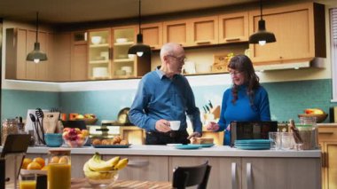 Emekli çift tost makinesinden tost makinesiyle kahvaltı hazırlıyor, tezgahın yanında yan yana duruyorlar. Kadın ve erkek bir anın tadını çıkarıyorlar. Emeklilik hayatı boyunca sohbet edip kaynaşıyorlar. Kamera A.
