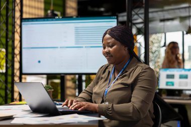 Siyahi kadın girişimci, gerçek zamanlı veri içgörüleri tarafından bilgilendirilip masasındaki günlük işleri çözen bir rapor yazar. Sürekli kalkınma ve ilerleme sağlama amaçlı stratejik düşünce ve hırs.