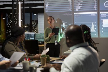 Konferans odasında proje ayrıntılarını ve zaman çizelgelerini sunan kadın danışman, rekabetçi bir iş ortamında hedeflere ulaşmak için bütçe ve operasyon planı oluşturuluyor.