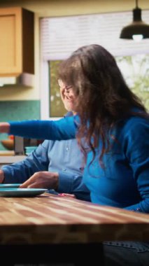 Dikey Video Olgun çift kahvaltı servisi yapıyorlar. Hamur işi, sıcak kahve, parlak mutfak masası. Sakin bir sabah rutini ve rahat bir emeklilik hayatı içinde sohbet ve kaynaşma. Kamera.