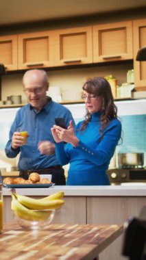 Dikey Video sunucusu karısı evde parlak bir mutfakta durmuş kahve fincanının keyfini çıkarıyor ve huzur içinde dinleniyor. Yaşlı kadın emekliler pozitif emeklilik, sakin yaşam ve neşeli anlar yaşatıyor.