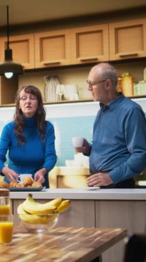 Dikey Video Yaşlıları mutfak tezgahında pasta ve ekmekle dinlenerek ev hayatının tadını çıkarıyorlar. Mutlu bir yaşam tarzında çalışan evli bir çift, rahat bir yaşam ve huzurlu bir emeklilik.