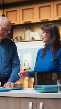 Dikey Video sunucusu çift modern mutfakta kahvaltı hazırlıyor, rahat bir sabah rutini. Karı koca mutfak tezgahında samimi bir anı paylaşıyor, sağlıklı yemek ve sıcak kahve servisi yapıyorlar.