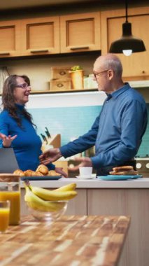 Dikey Videoda gülümseyen yaşlı karı koca mutfakta romantik bir dansı paylaşıyor, tutkulu bir aşk şarkısında vals yapıyor ve birbirleriyle flört ediyorlar. El ele tutuşmak ve yavaşça dans etmek, sallanmak