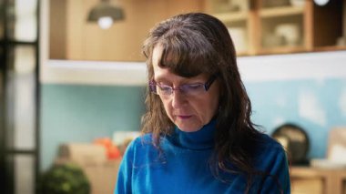 Mutfakta gülümseyen ve sıcak içkinin keyfini çıkaran son sınıf kadınının portresi. Emekli hayatın doğal portresi huzurlu yaşam tarzını ve evdeki konforu yakalar. Kamera B.