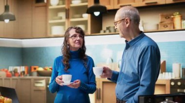 Apartmanının mutfağında rahat yaşam tarzının keyfini çıkaran neşeli yaşlı insanlar. Yaşlı çift huzur içinde gülümsüyor. Sağlıklı refahı ve emeklilik yaşının dengeli zevkini yansıtıyor. Kamera B.