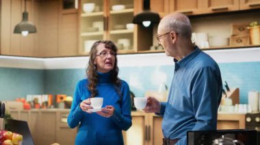 Mutfakta emekliliğin tadını çıkaran, tezgahın yanında gülümseyen ve kahve servisi yapan son sınıf mutlu çiftin portresi. Olgun insanlar neşeli yaşam tarzı ve refah için rahat anları kucaklarlar. Kamera B.