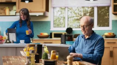 Kıdemli erkek ve kadın zaferi kutluyor. Heyecanlı tebessümlerle tezahürat yapıyor, kahvaltı ve kahve içerken sohbet ediyorlar. Olgun çiftler, emeklilik hedefleri için samimi bir başarı anının tadını çıkarırlar. Kamera B.