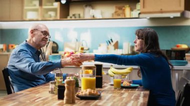 Yaşlı çift, sağlıklı ev yapımı kahvaltıyla, hamur işi yiyerek ve kahve içerek doğal sabah rutininin tadını çıkarıyor. Karı koca samimi bir an için gündelik bir konuşma yapıyorlar. Kamera B.