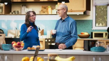 Olgun bir çift kahve servisi yapıyor ve mutfakta gülümsüyor. Huzurlu aile rutininin tadını çıkarıyorlar. Doğal ifadeler neşeli yaşam tarzını, refahı ve birlikte emekliliği yansıtıyor. Kamera B.