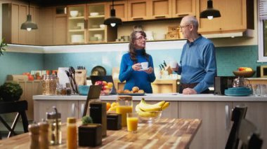 Mutfakta emekliliğin tadını çıkaran, tezgahın yanında gülümseyen ve kahve servisi yapan son sınıf mutlu çiftin portresi. Olgun insanlar neşeli yaşam tarzı ve refah için rahat anları kucaklarlar. Kamera A.