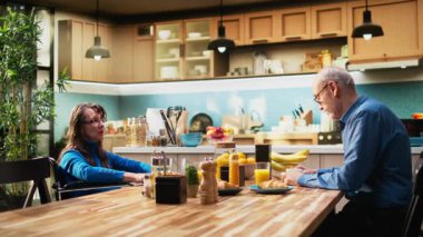 Engelli bir kadın ve kocası mutfak masasında kahve servisi yapıyor ve sohbet ediyorlar. Emeklilik çağındaki sağlıklı yaşam tarzını ve rahatlığını yansıtıyorlar. Yaşlı çiftler sohbet eder. Kamera A.