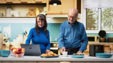 Üst düzey evli çift, kahve fincanlarıyla sessiz mutfak anlarından hoşlanırlar, dizüstü bilgisayarlarına bakarlar ve web sitelerine bakarlar. Huzurlu bir emeklilik, pozitif bir yaşam tarzı ve rutinin keyfi. Kamera B.
