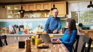 Evli insanlar sohbet ediyor ve mutfaktaki dizüstü bilgisayardan haberleri kontrol ediyorlar, taze kahve içiyorlar ve evde sohbet ediyorlar. Rahat bir aile sabahında sıradan bir an. Kamera A.