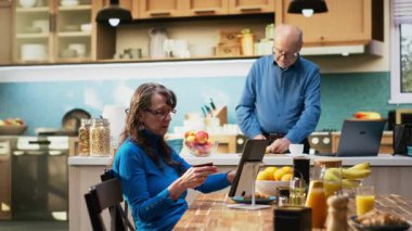 Elinde kredi kartıyla online alışveriş yapan yaşlı bir kadın, dizüstü bilgisayarındaki e-ticaret uygulama arabasındaki erzak ve temel ihtiyaçların listesini gözden geçiriyor. Müşteri kimlik bilgilerini kontrol ediyor. Kamera B.