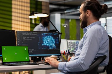 Yapay zeka algoritmalarını kodlamak için yeşil ekran tableti kullanan teknisyen teknoloji firması ofisindeki yazılım hatalarını düzeltiyor. Çalışan adam krom anahtar aygıtı kullanarak sistem istikrarını geliştiriyor