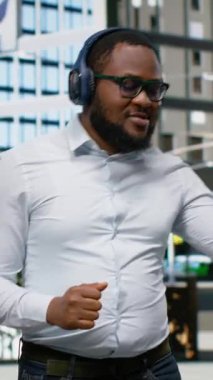 Dikey Video Yetişkin erkek güvenli bir şekilde yürüyor ve şehir kaldırımında havalı şarkılar söyleyerek dans ediyor, tasasız funky adam müzik dinliyor ve şehir merkezindeki bir caddede havalı dans hareketleri sergiliyor. Kamera B.