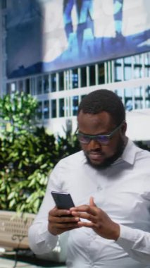 Dikey Video Siyah Adam, şehir merkezinde yürürken cep telefonunda uygulamaları tarıyor, hareketli bir enerji, kalabalık bir şehir içinde güçlü bir şahsi varlık yaratıyor ve parkın yakınında kentsellik yaratıyor. Kamera A.