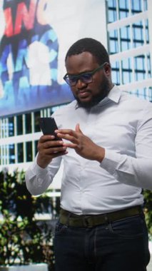 Dikey Video Yetişkin Erkek, şehir merkezindeki yeni başarısından gurur duyuyor. Şehir merkezindeki kaldırımda heyecanlı ve tezahürat yapıyor. Akıllı telefonundan iyi haberler okuyan bir adam. Kamera A.