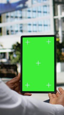 Kentsel parktaki bir bankta oturan Afro-Amerikan malı dikey video krom anahtar tablet üzerinde kendine güvenen bir tavırla çevrimiçi görevleri daktilo ediyor ve yönlendiriyor. Mimari ve canlı şehir hayatı