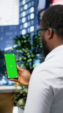 Şehir merkezindeki kaldırımda yetişkin bir adamla dikey video yeşil ekran akıllı telefon, hareketli manzarası ve gökdelenleri olan kalabalık metropol alanı. Şehir merkezindeki modern şehir hayatı. Kamera B.