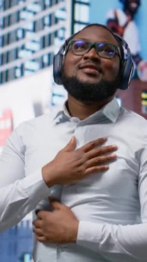 Dikey Video Trendi Afrikalı Amerikalı adam en sevdiği müzikle şarkı söylüyor ve dans ediyor, sokakta kulaklıkla harika dans hareketleri yapıyor. Kendine güvenen sokak tarzı ve şehir hayatının akışı. Kamera B.