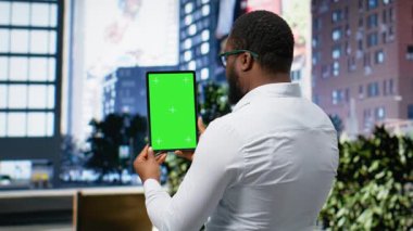 Dikey yeşil ekran, elinde tablet olan siyah bir adam şehir merkezinde şehir merkezindeki şehir ışıklarının altında gökdelenlerin yanında geziniyor. Metropolitan bölgesi. Kamera B.