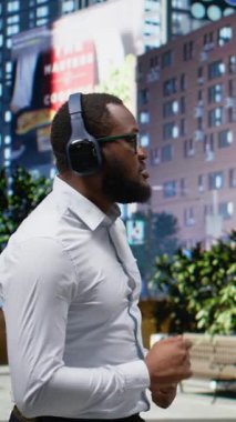 Dikey Video Kendinden emin zenci adam kaldırımda dans ediyor, modern bir şehir caddesinde yürüyor ve kulaklıkla müziğin tadını çıkarıyor. Canlı metropoliten manzara, şehircilik gibi. Kamera A.