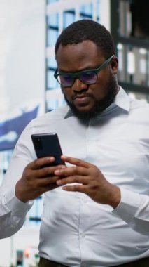 Dikey Video Siyah Yetişkin mutlu ve mutlu olarak telefon ekranında iyi haberlerle şehir merkezinde bir caddede yürüyor ve başarının tadını çıkarıyor. İnsan başarıyla heyecanlanır ve tatmin olur. Kamera B.