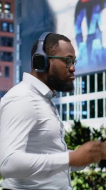 Dikey Afrikalı Amerikalı adam dans ediyor ve sokakta müzik dinliyor, kulaklık takıyor ve şehir kaldırımında neşeli hissediyor. Şık şarkıların ve şehir merkezinde imza günlerinin tadını çıkarıyorum.