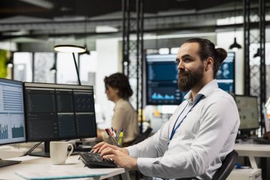 Modern çalışma alanındaki profesyonel erkek yönetici bir bilgisayar monitöründe öngörü ve iş stratejisini analiz ederek, üretkenlik için rapor yazmayı ve planlamayı güvence altına alır.