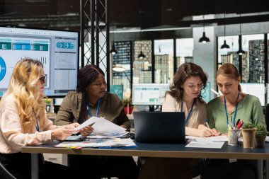 Çeşitli iş arkadaşları güçlü bir başlangıç oluşturarak iş stratejisini, dizüstü bilgisayardaki performans verilerini ve başarı, ilerleme ve ortak hedefler etrafında sıralanmış belgeleri analiz ederler..