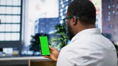 Yoğun şehir merkezinde siyahi bir adamla dikey krom anahtar ekranı, şehir merkezinde gökdelenlerin ve ofis binalarının yakınındaki kaldırımda yürüyor. Metropolitan bölgesi. Kamera B.