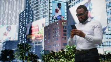 Çevresi mimari, ufuk çizgisi ayrıntıları ve çağdaş şehir hayatının dinamik kültürüyle çevrili kaldırımda ilerleyen Afrikalı Amerikalı yetişkin yazı ve mesajları. Kamera A.