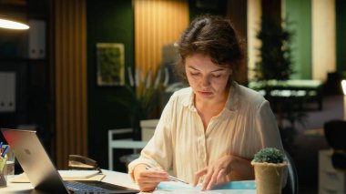 Mesai saatleri dışında karanlık bir ofiste rakamları ve finans rakamlarını araştıran yönetici, güncellemeleri belgeliyor ve iş sunumu gündemini düzenliyor. Hedefleri gece belirliyorum. Kamera B.