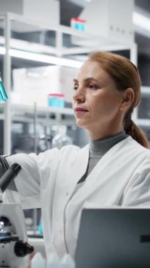 Laboratuvardaki dikey video bilimci analiz etmek için mavi sıvıyı test tüpüne koyuyor. Laboratuvar çalışanı spektroskopik analize hazırlanmak için kimyasal örnek aktarıyor. Kamera B.