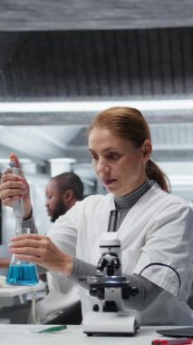 Dikey video test geliştirme uzmanı laboratuvar pipetleme mavi sıvıyı test tüpüne koyup analiz ediyor. Moleküler biyolog, spektroskopik analize hazırlanmak için kimyasal örnek aktarıyor.